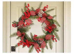 Détail de couronne de Noël avec baies rouges, pommes de pin et nœuds à carreaux sur porte