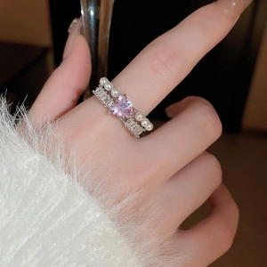 Gros plan d'une bague ouverte avec pierre rose en cœur et perles sur le doigt
