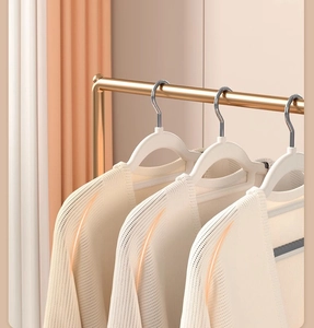 Close-up of white anti-slip hangers with silver hooks holding a knitted cardigan on a gold rod