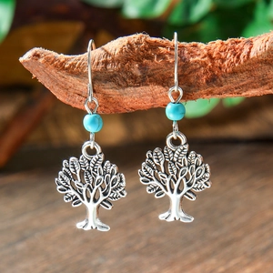 Macro detail of silver Tree of Life earrings with a turquoise bead on natural wood