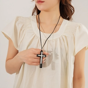 Detail of a leather cord necklace with a wood double cross pendant worn by a model