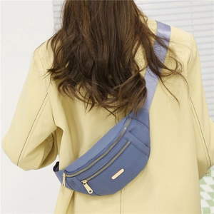Rear view of a model wearing a blue nylon fanny pack with golden zippers and broad strap