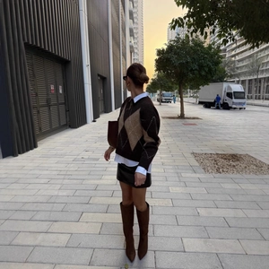 Women's brown argyle knit sweater paired with white shirt and black leather mini skirt