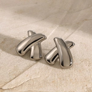 Macro shot of silver polished crisscross stud earrings on textured beige stone