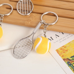 Detail of silver tennis racket pendant and yellow ball keychain on wooden tray
