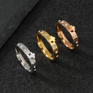 Close-up of silver, gold and rose gold cross rings with pavé rhinestones on black surface