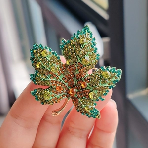 Close-up of maple leaf brooch with multicolored green and orange crystals on gold alloy