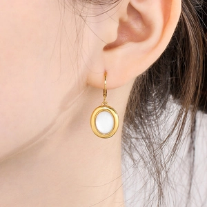 Close-up of a gold oval earring with a white stone inlay on a model's ear