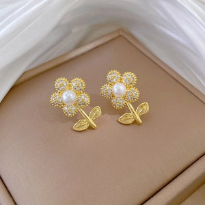 Close-up of golden floral stud earrings featuring center pearls and crystal pavé petals