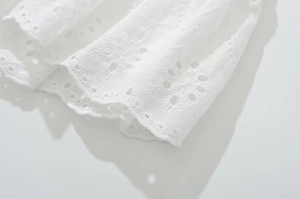 Close-up of white eyelet lace fabric with intricate embroidery and hollow patterns