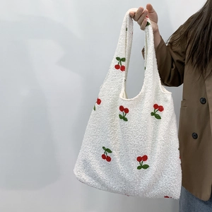 Detail of white lamb wool tote bag with red cherry embroidery held by a model