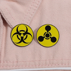 Macro detail of biohazard and radiation symbol metal enamel pins on pink fabric texture