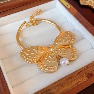 Elegant gold butterfly bracelet with embossed texture and white pearl pendant on display