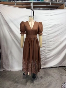 Détail de broderie sur robe longue marron à col en V et manches bouffantes sur mannequin