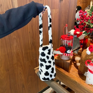 Close-up of plush cow print water bottle bag with crossbody strap in a cozy setting