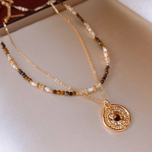 Detail of double-layer gold compass necklace with tiger eye stone and beaded chain