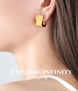 Macro shot of gold-plated geometric square huggie earrings worn on a model's ear