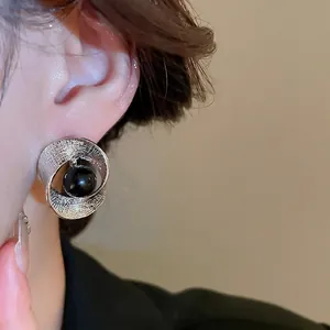 Minimalistischer silberner gedrehter Metallohrring mit einer glänzenden schwarzen Perle