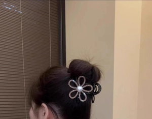 Detailed view of sparkling sunflower rhinestone hair claw clip with center pearl on dark hair