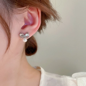 Detailed close-up of bow knot stud earring with white pearl drop on female ear