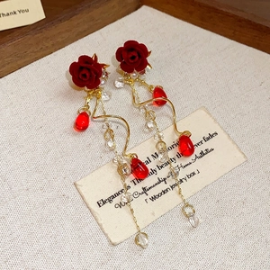 Detail of red velvet rose earrings with long gold tassel and pear-shaped red drop beads