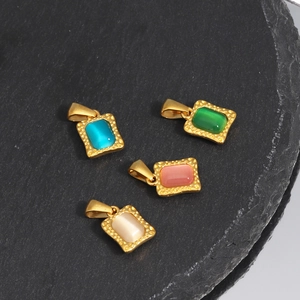 Square gold stainless steel pendants set with colorful cat-eye stones on a stone surface