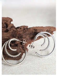Detail of silver double-layered C-shape earrings with twisted and smooth metal texture