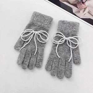 Detail view of grey knit gloves featuring decorative white pearl bow accents