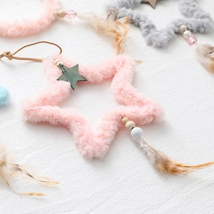 Plush star Christmas ornaments with wooden beads and feathers on white textured background