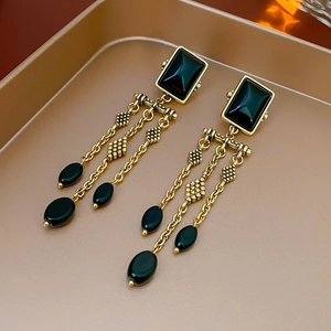 Detail of vintage long earrings with gold chains, black square gems, and oval beads
