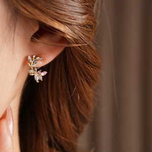 Close-up of golden leaf stud earring with colorful zircon crystals on model