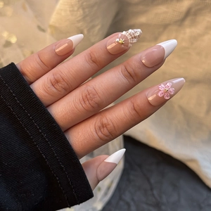 Macro shot of 3D pink flowers and pearl accents on nude French almond press-on nails