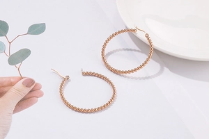 Detail of rose gold beaded hoop earrings with small spheres on a white minimalist surface