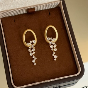 Détail de boucles d'oreilles ovales dorées à franges et cristaux dans un écrin