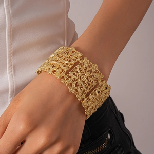 Gros plan d'un large bracelet doré avec des motifs de fleurs ajourés et détaillés