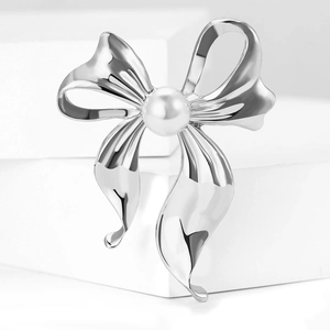 Macro detail of silver bow brooch with a central pearl on a white pedestal display