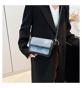Close-up of light blue denim handbag with black leather trim and metal buckle detail