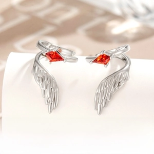 Macro shot of silver wing-shaped ear cuffs with red kite-cut gemstones on a white stand