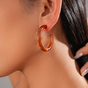 Close-up of model wearing an amber acrylic C-shaped hoop earring with a glossy finish