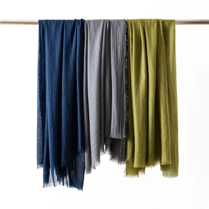 Detailed view of navy, grey, and green linen scarves with fringe edges on a rack