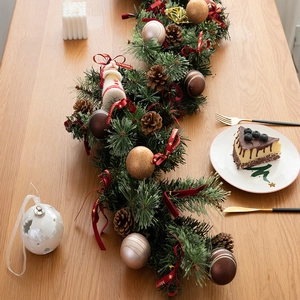 Lush Christmas garland with pine cones and red ornaments on a rustic wooden dining table