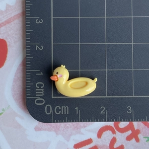 Mesure détaillée de la taille d'un accessoire en résine canard jaune sur un tapis