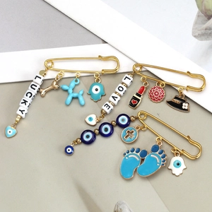 Close-up of golden safety pin brooches with Evil Eye, Fatima Hand and heart charms