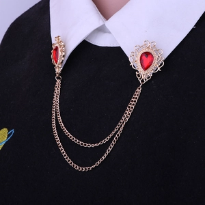 Detail of vintage gold collar pin with red gemstones and tassel chains on shirt