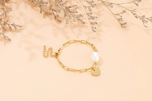 Détail du bracelet chaîne trombone avec une grande perle et un pendentif cœur doré poli