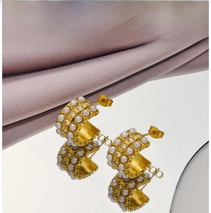 Detail of gold C-shape hoop earrings with white pearls and clear cubic zirconia on silk