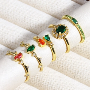 Detailed set of five gold rings with emerald and ruby gemstones on jewelry stands