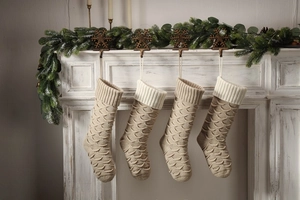 Close-up of four cream knitted Christmas stockings with cable knit patterns on a mantel