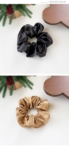 Detail of elegant black and gold-brown leather texture scrunchies on a wooden tray