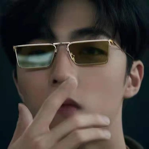 Close-up of rectangular metal sunglasses with gold frames and amber lenses on a model